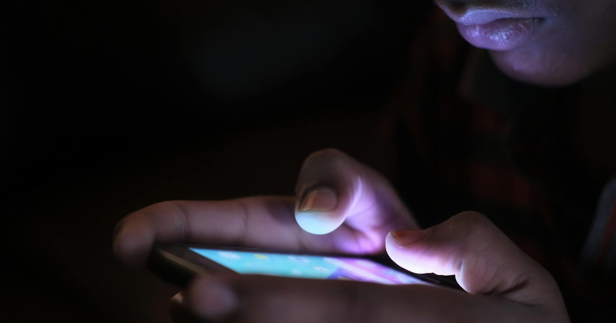 Close-up of a person holding and using an illuminated smartphone in a dark setting.