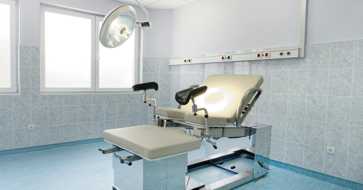Bright gynecological examination room with adjustable chair and overhead light in a medical facility.