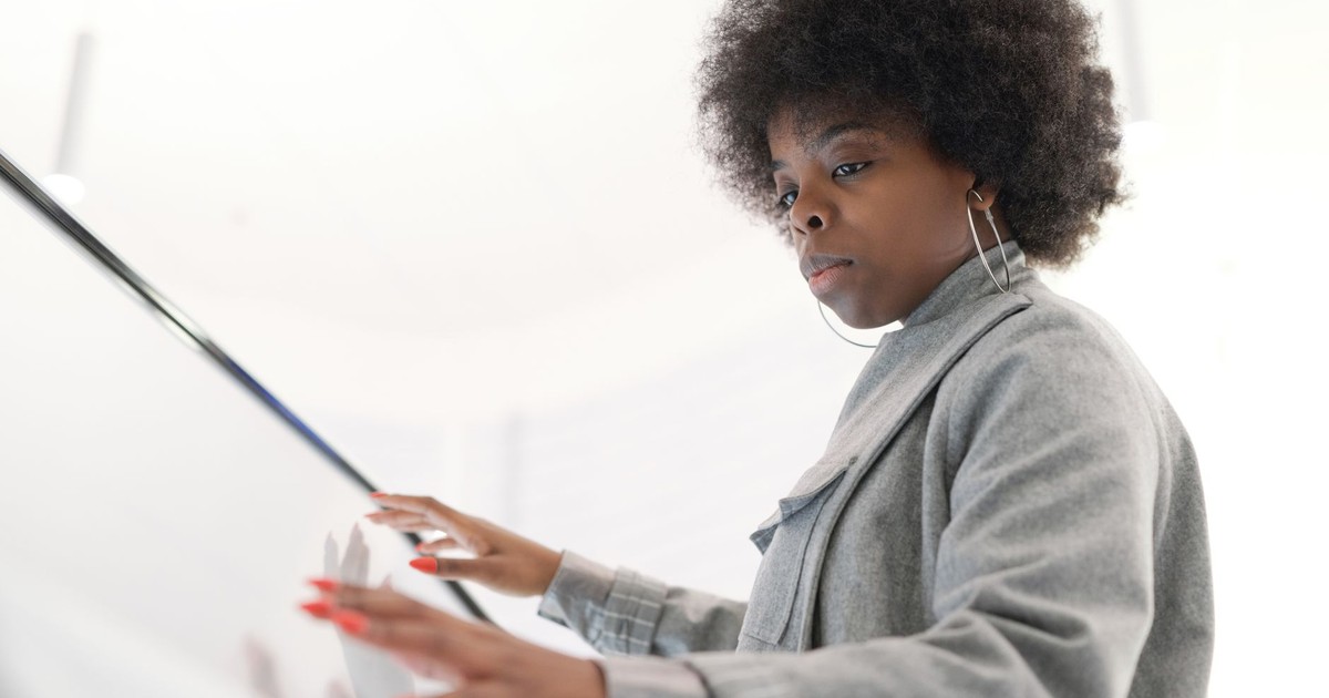 A fashionable woman with afro hair interacts with a digital touchscreen indoors.