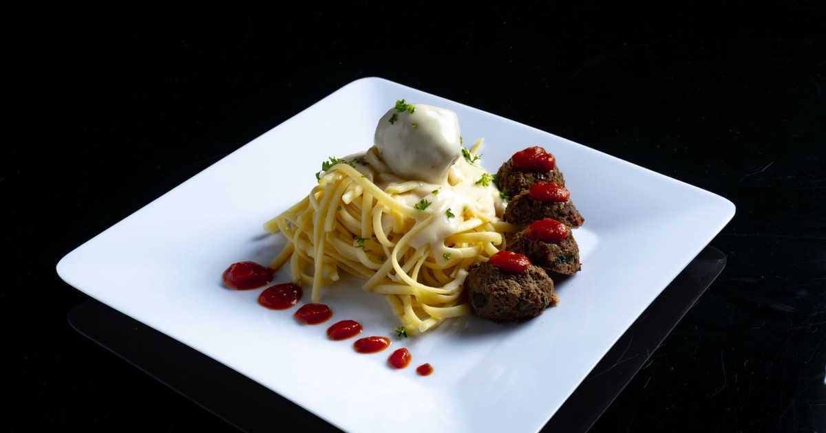 A gourmet dish featuring spaghetti with creamy sauce and meatballs served on a white plate.