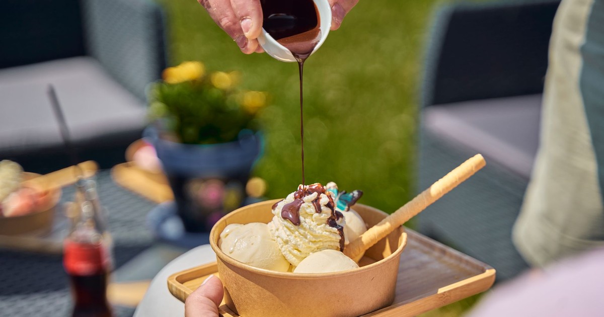 Close-up of chocolate sauce being poured over a bowl of vanilla ice cream outdoors.