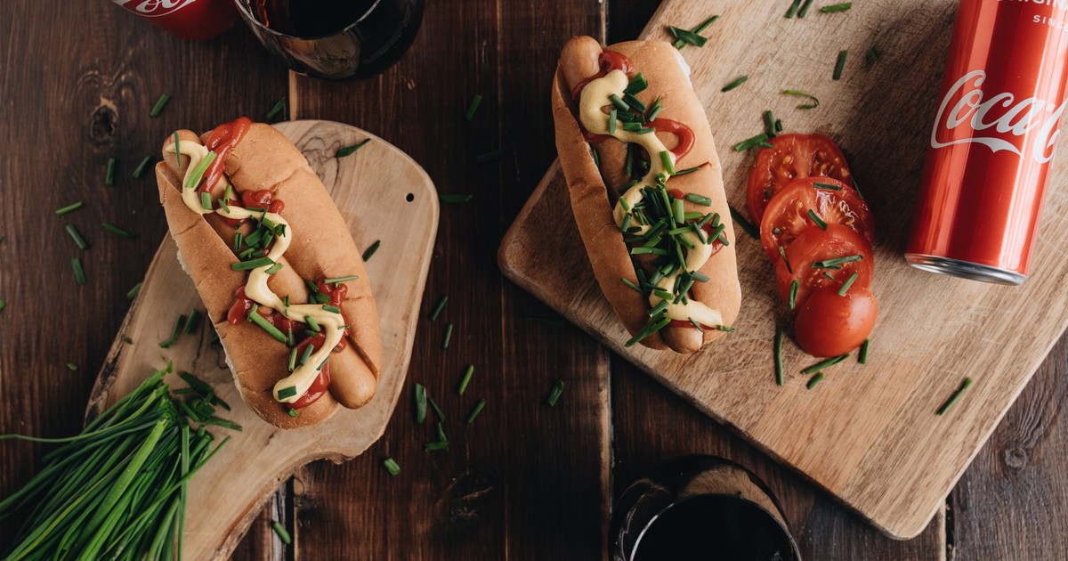 Flat lay of hot dogs and Coca-Cola cans on wooden boards. Vibrant and appetizing presentation.
