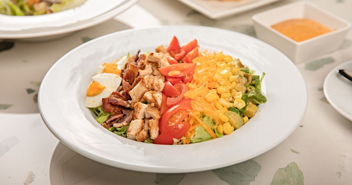 A vibrant Cobb salad with chicken, eggs, bacon, cheese, and vegetables on a table.