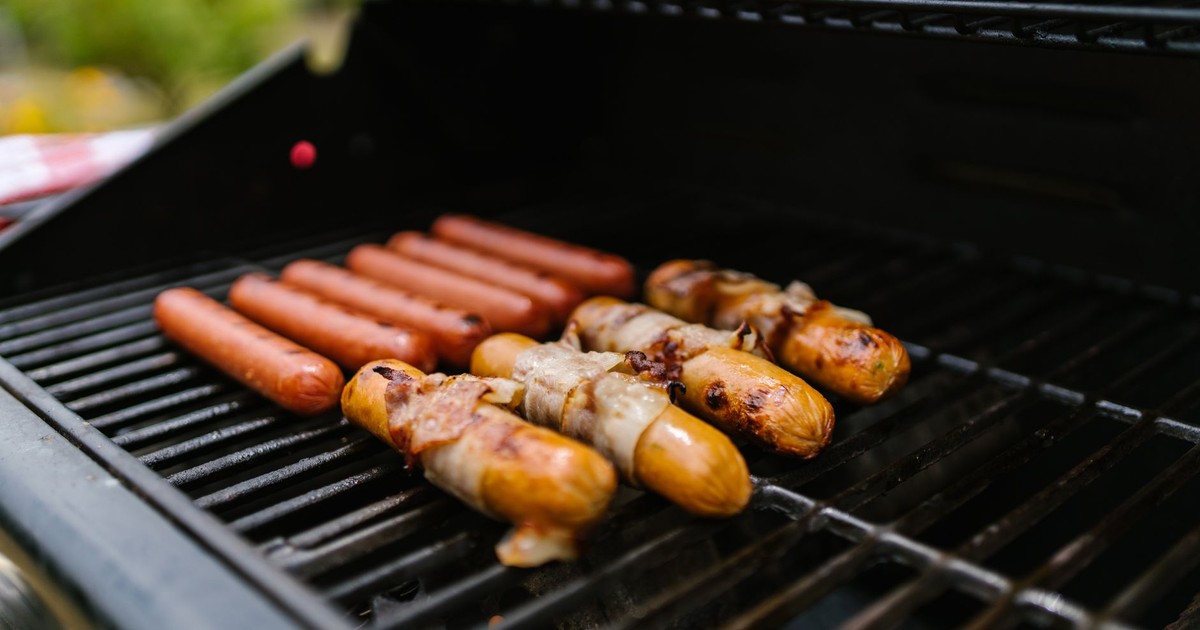 Close-up of hotdogs and bacon-wrapped sausages on a grill outdoors.