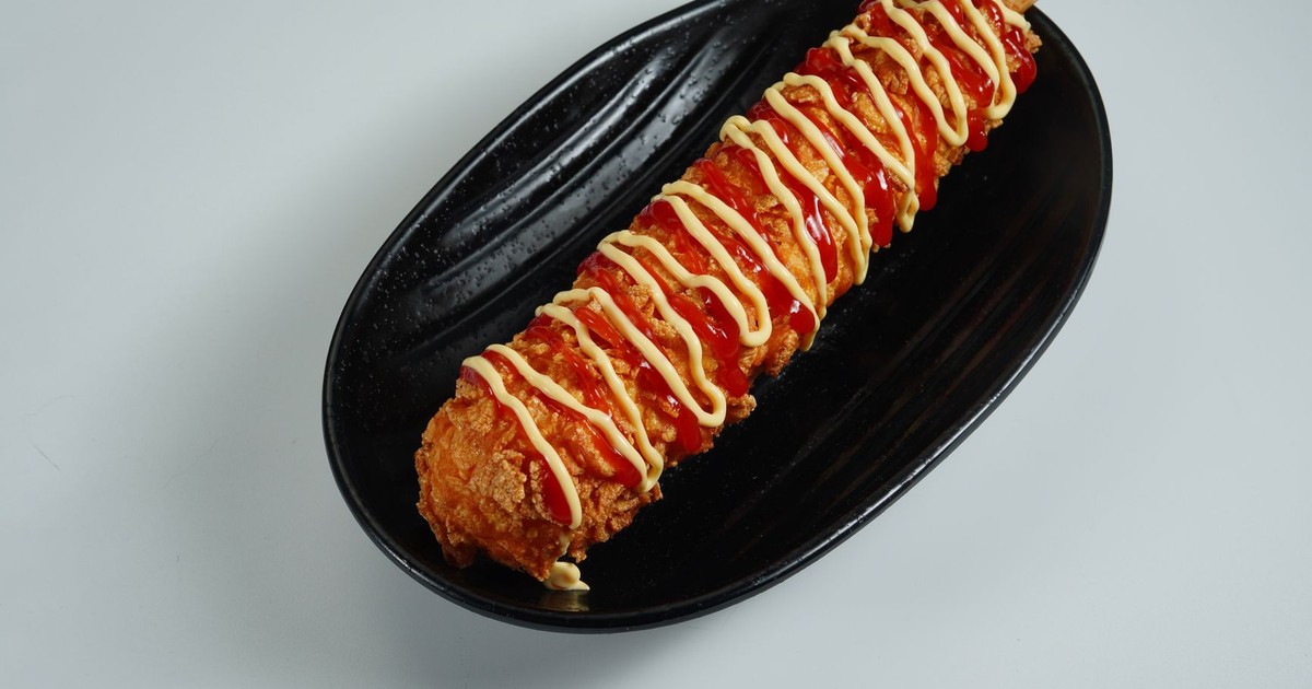 Close-up of a Korean corn dog drizzled with ketchup and mustard on a black plate.