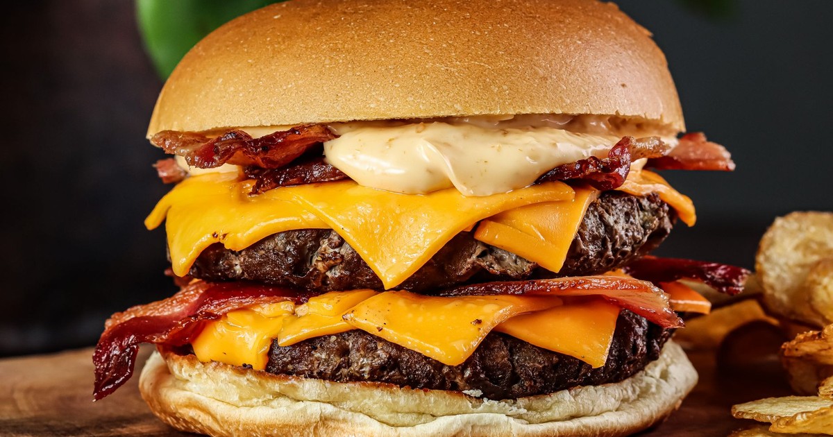 Close-up of a mouth-watering bacon cheeseburger with a toasted bun and crispy chips.