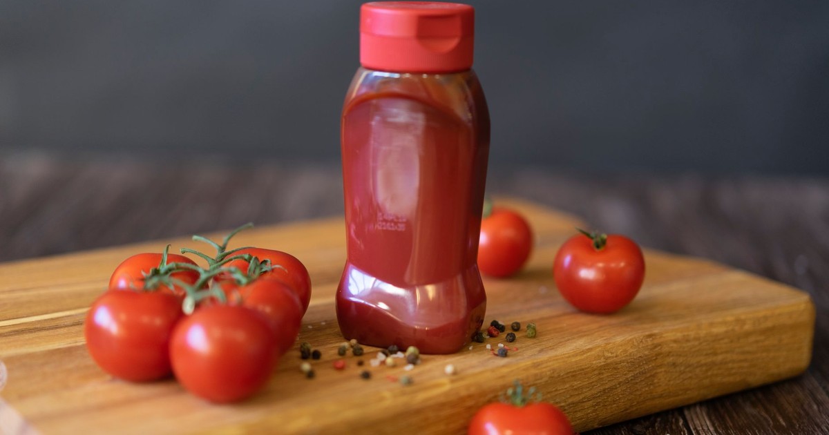 Close-up of tomatoes and ketchup bottle on a wooden board with peppercorns.