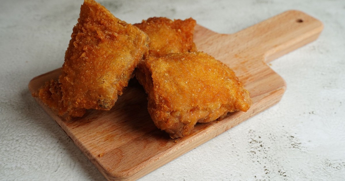 Three pieces of golden brown fried chicken on a wooden cutting board.