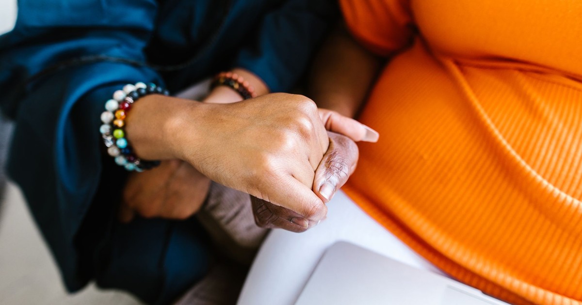 A close-up of two hands gently holding, symbolizing unity and support, with vibrant clothing in the background.