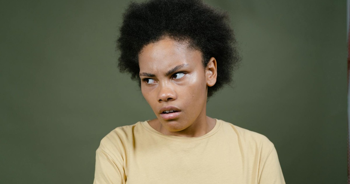 Close-up of a young woman with afro expressing a pensive mood against a green background.