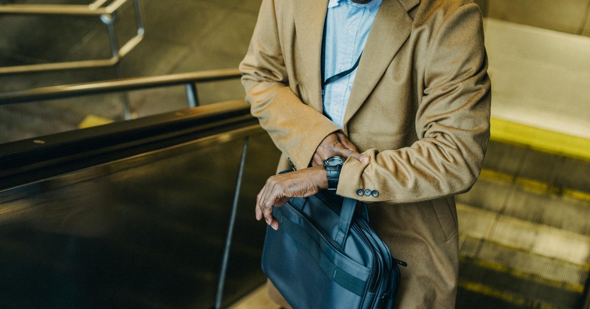 From above crop punctual African American businessman riding escalator and checking time on wristwatch while leaving metro station