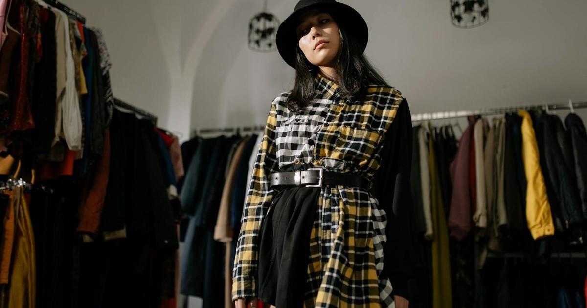 Stylish woman in a plaid outfit and hat posing in a vintage clothing store.
