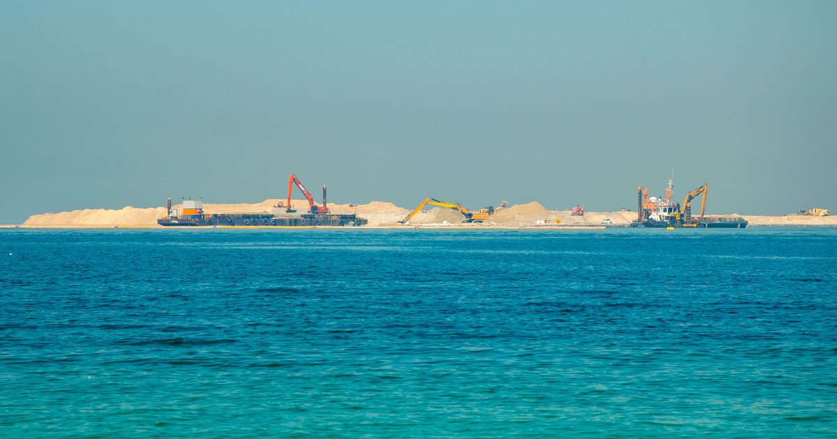 Distant view of an offshore construction site with machinery and clear blue sea.