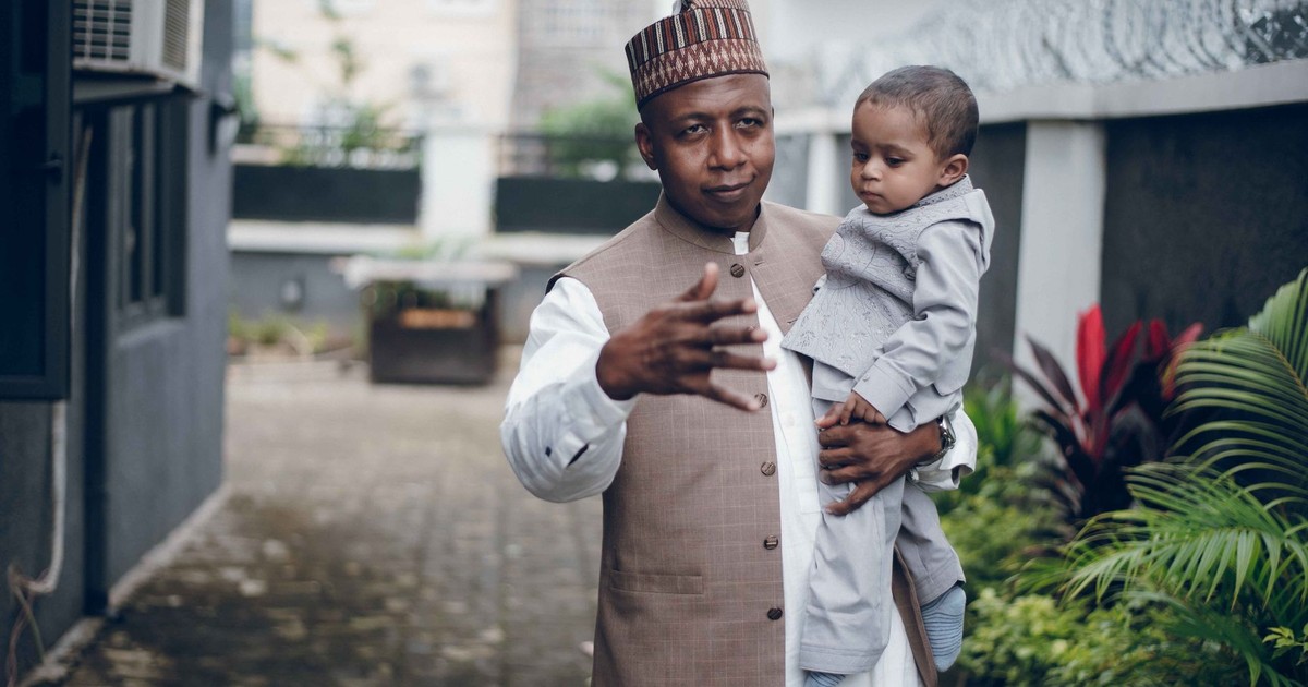 Father holding his young son outside in an urban environment, wearing traditional attire.
