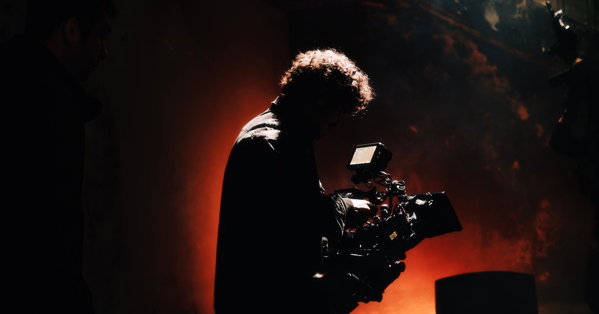 A professional cameraman captures footage in a creatively lit, moody setting, backlit by warm light.