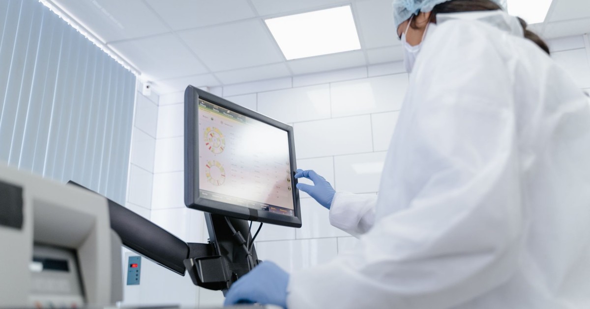 Woman in lab coat using touchscreen monitor in a modern laboratory setting.