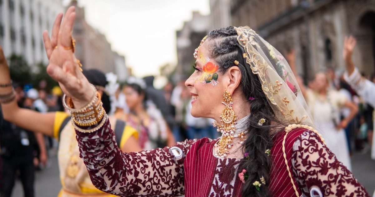 A woman in traditional attire performs a dance in a vibrant street festival setting.