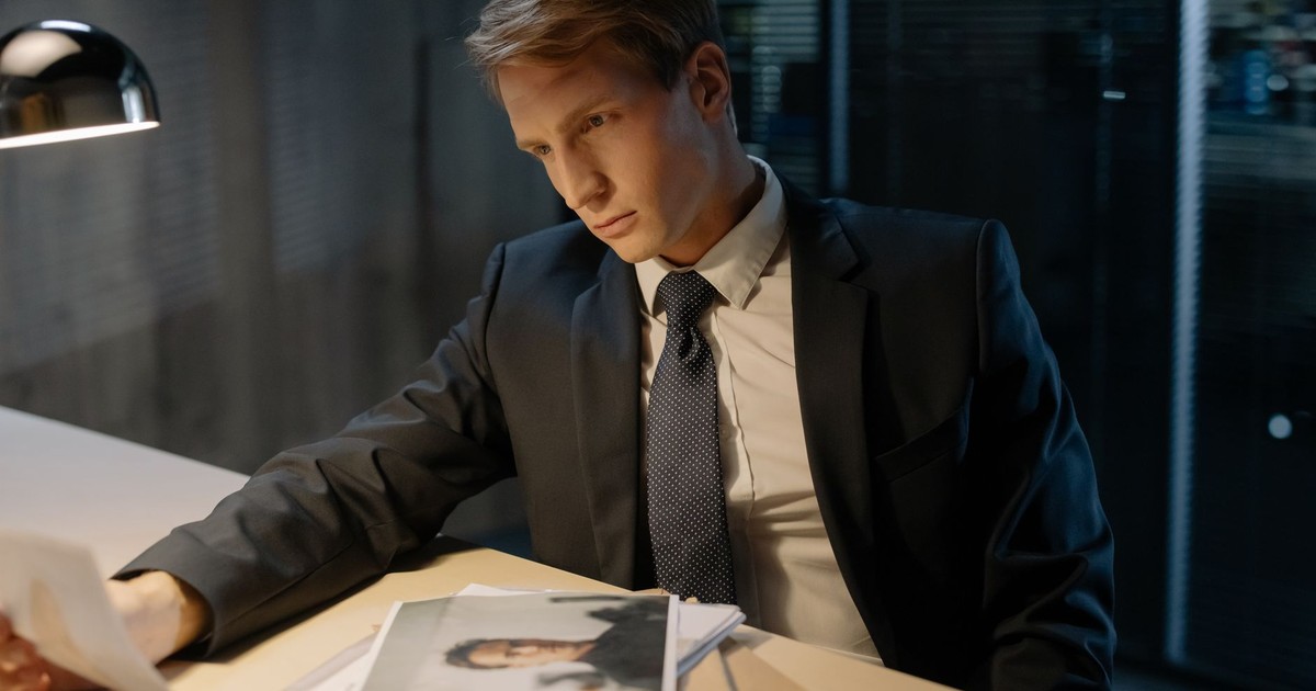 Serious male investigator analyzing documents under lamp light in office.