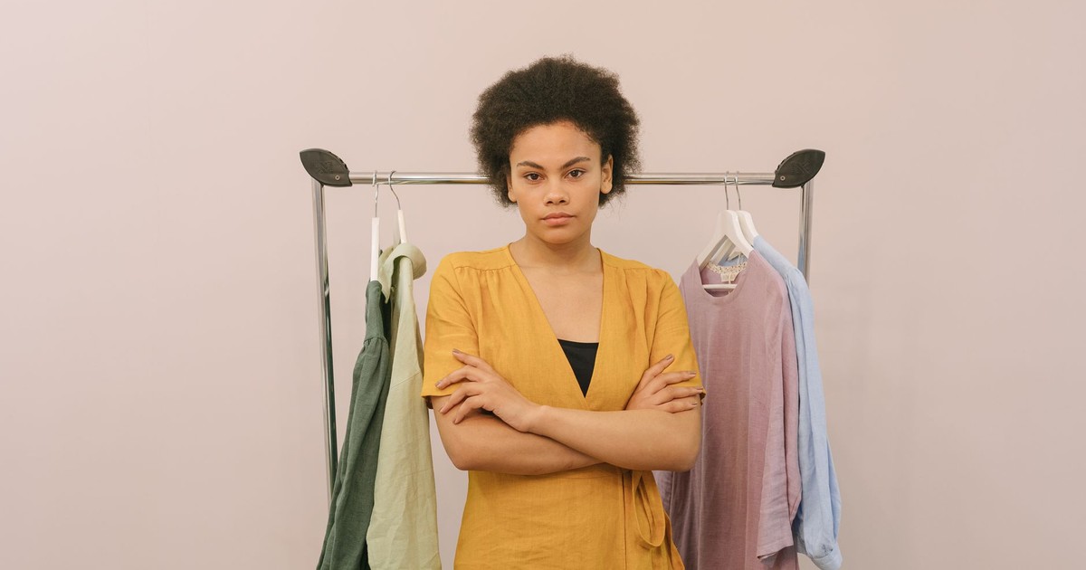 Woman with crossed arms standing by clothes rack indoors, exuding confidence and style.