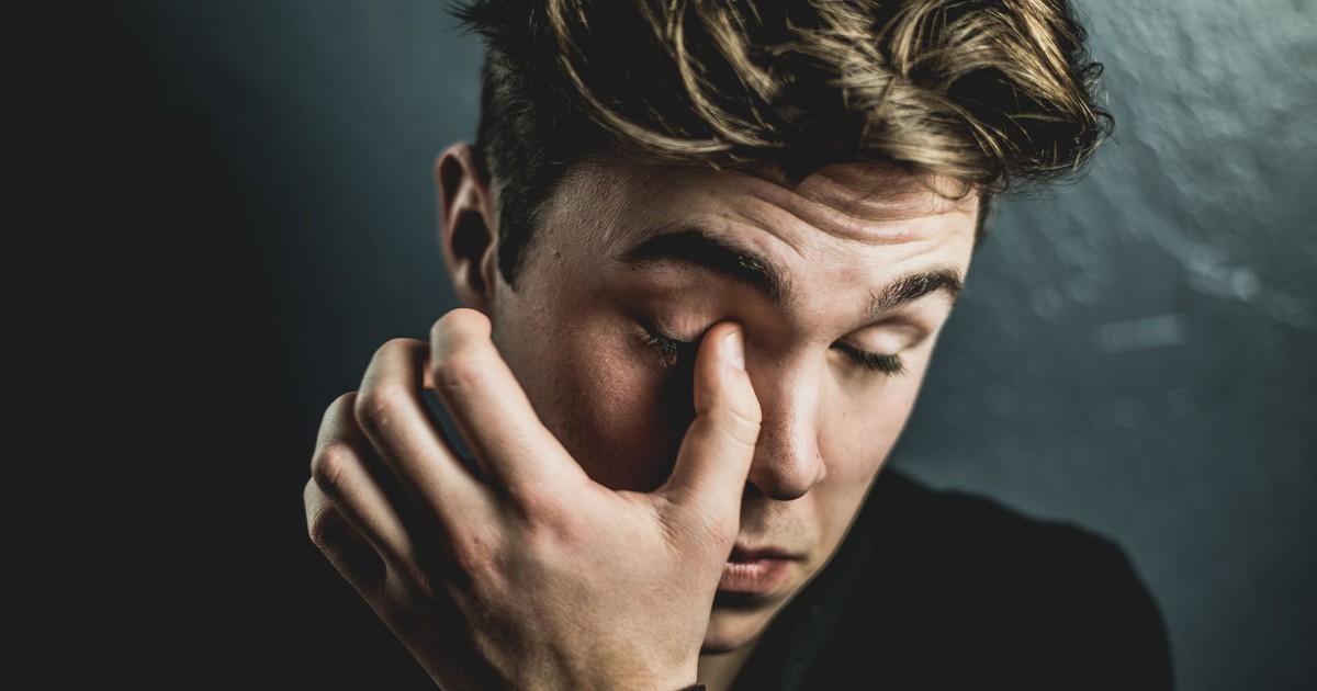 Close-up portrait of a thoughtful young man rubbing his eyes, conveying emotion and introspection.