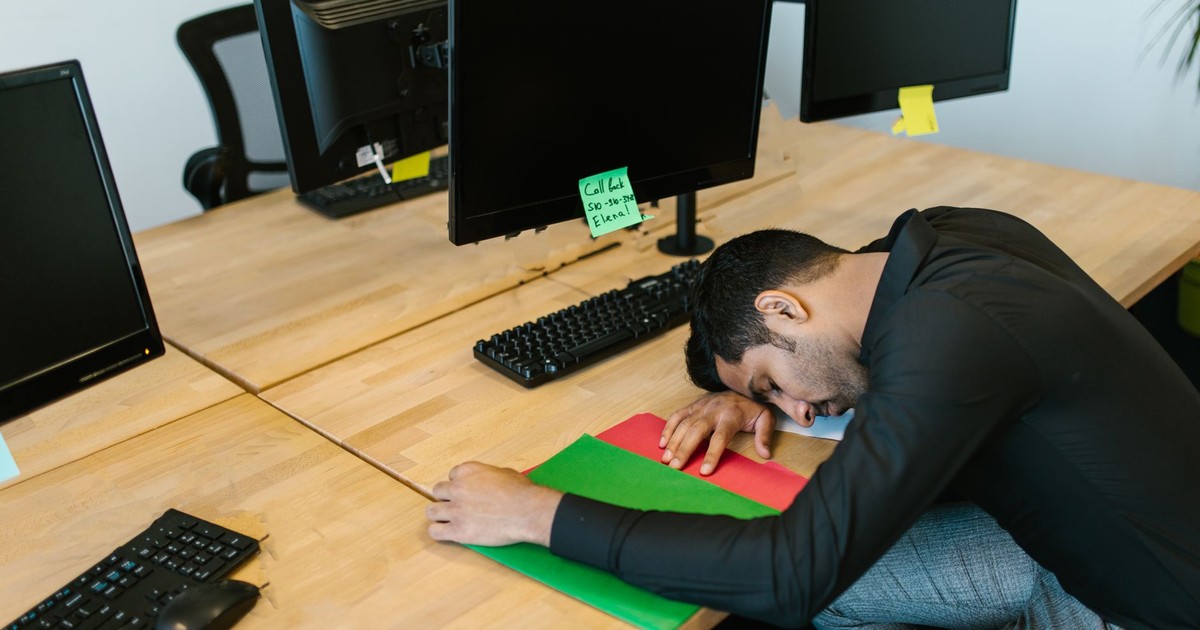 Exhausted office worker falling asleep at desk with monitors and keyboard.
