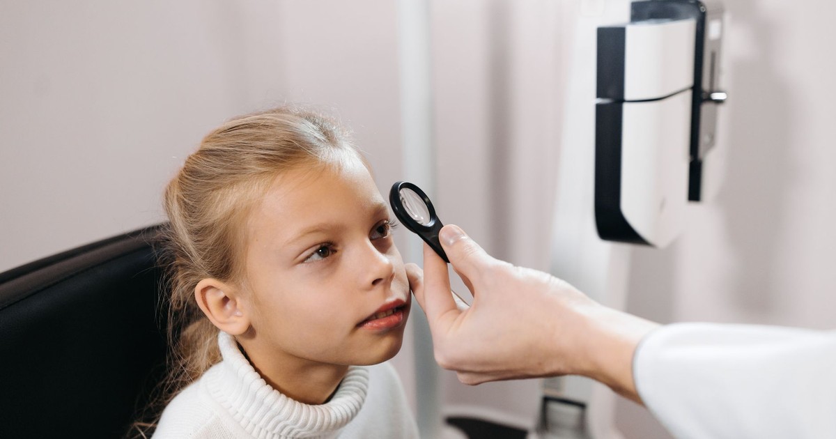 A young girl sitting in an ophthalmologist's office having her eyes examined.