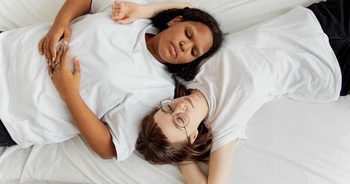 Two women in white shirts resting peacefully on a bed, expressing love and connection.