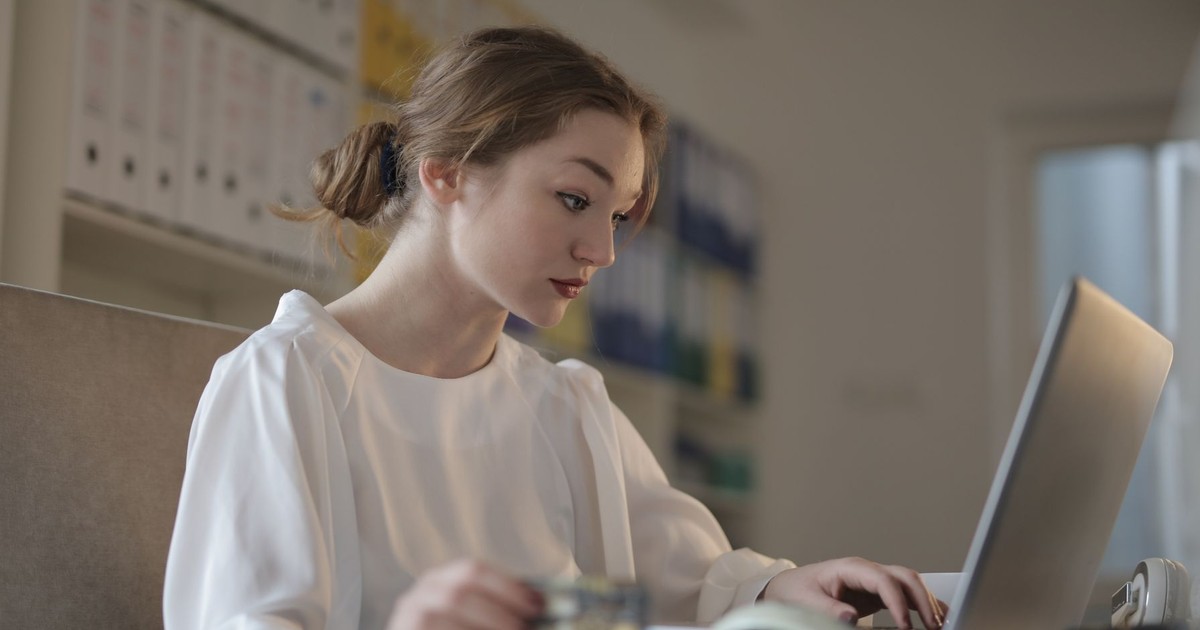 Focused woman in white working on a laptop in a modern office setting.