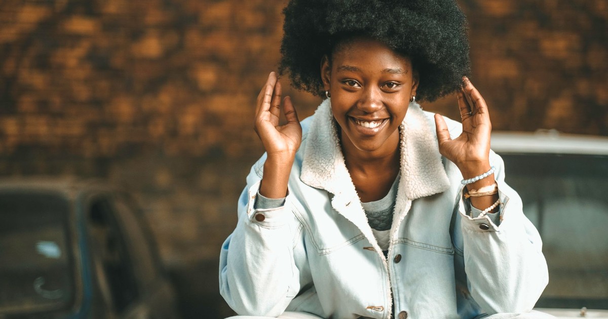 Happy young woman with afro hairstyle sitting outdoors, smiling and gesturing playfully.
