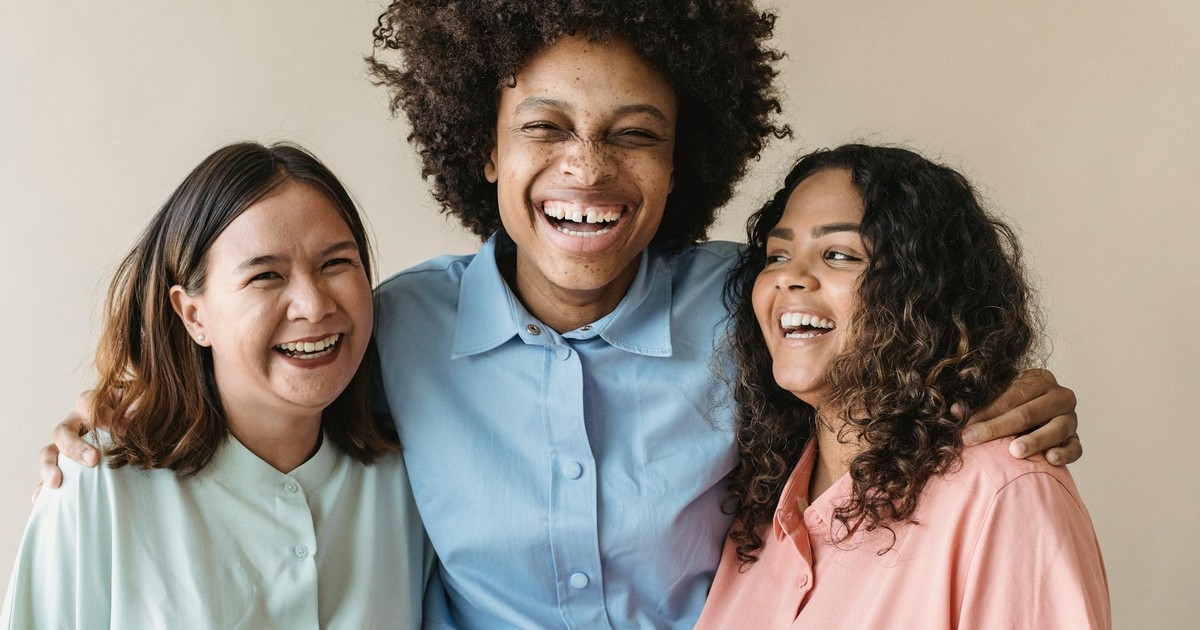 Three women of diverse backgrounds sharing a joyful moment, showcasing happiness and unity.