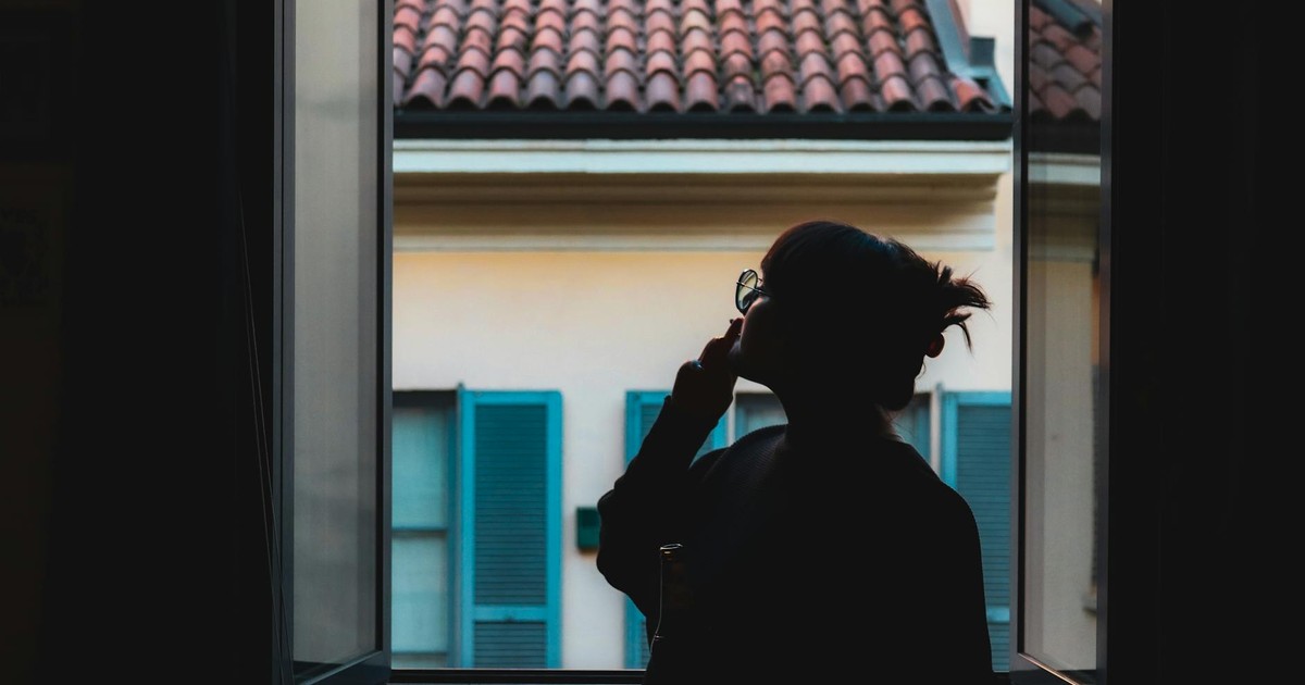 Silhouette of a woman in a serene moment by the window, viewing the tiled roof outside.