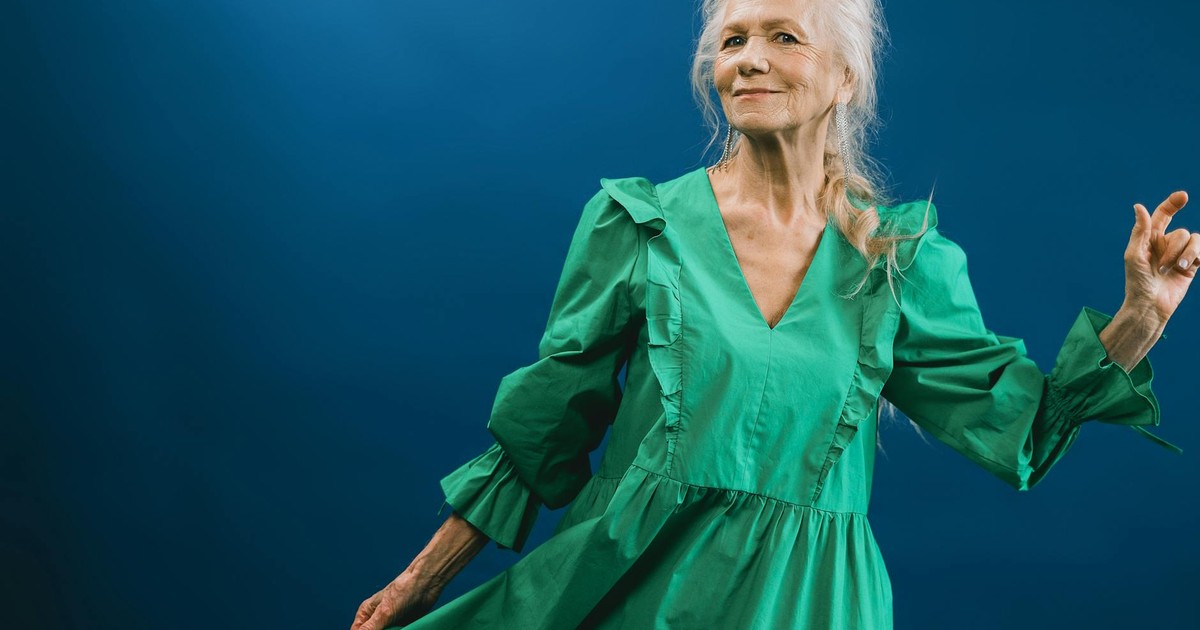 Portrait of an elegant senior woman in a vibrant green dress posing against a blue backdrop.