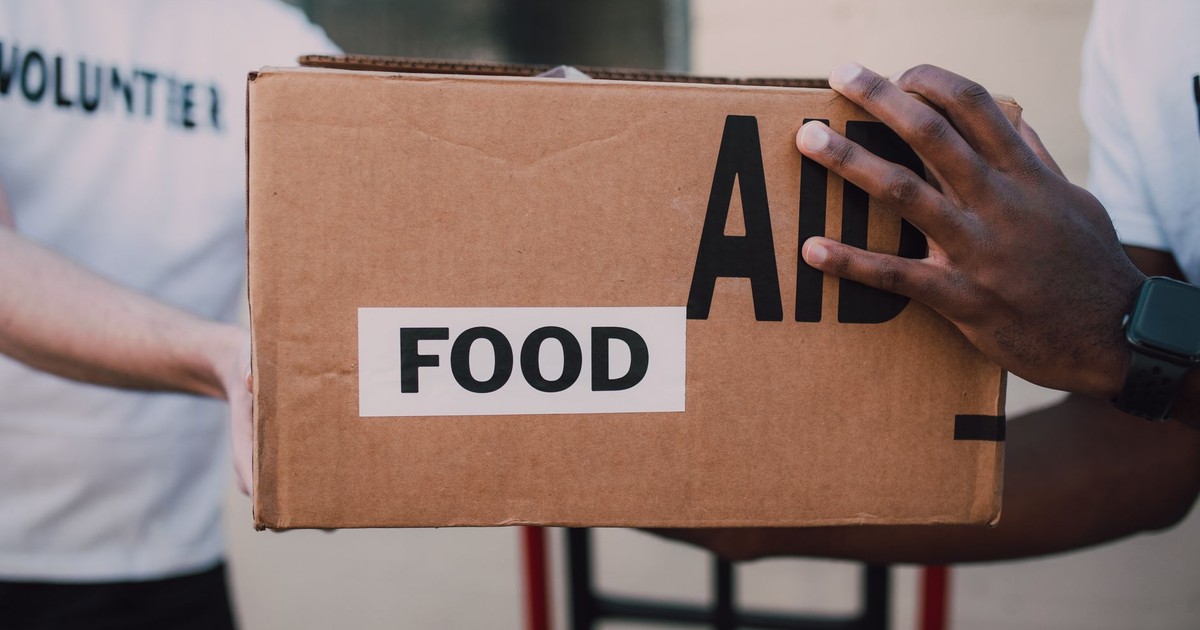 Two volunteers handing over a box labeled 'Food Aid', symbolizing community support.