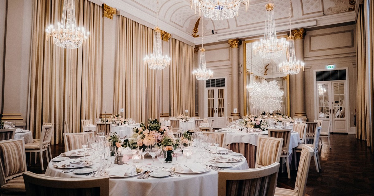 Luxurious ballroom setting with chandeliers, lavish decor, and elegantly arranged tables.