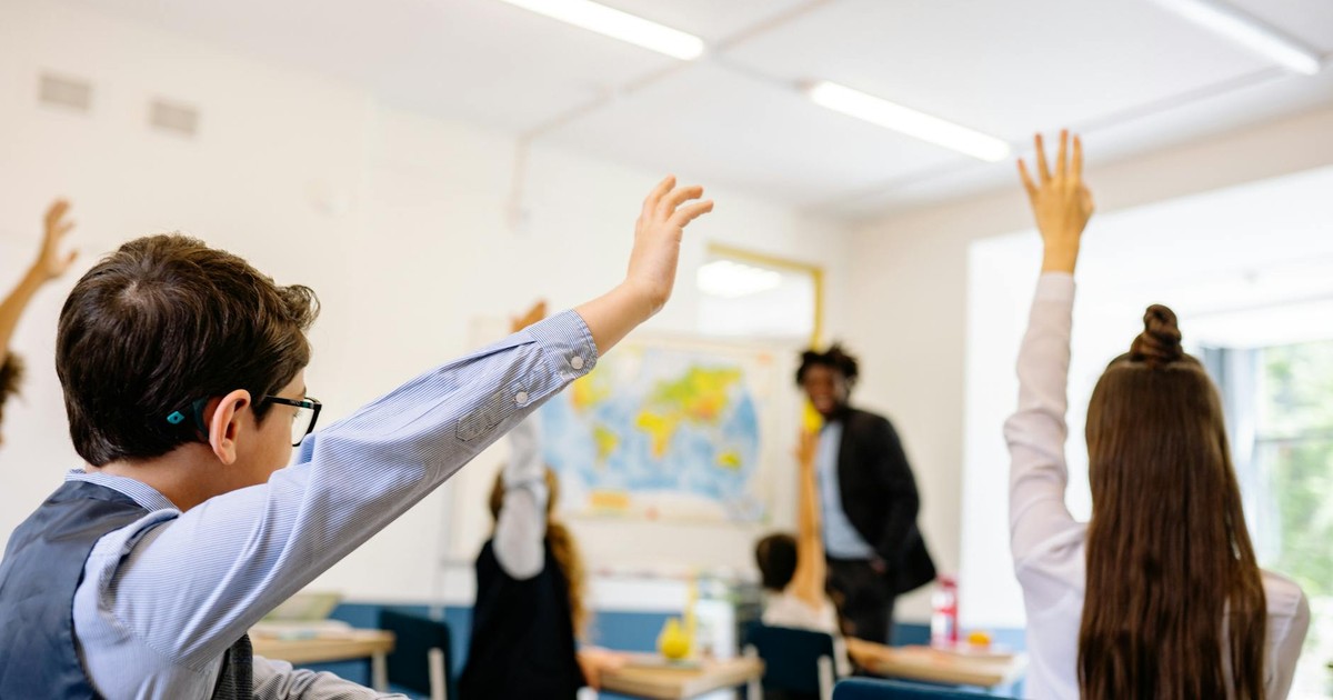 Enthusiastic students participating in a classroom, raising hands to answer teacher's question.