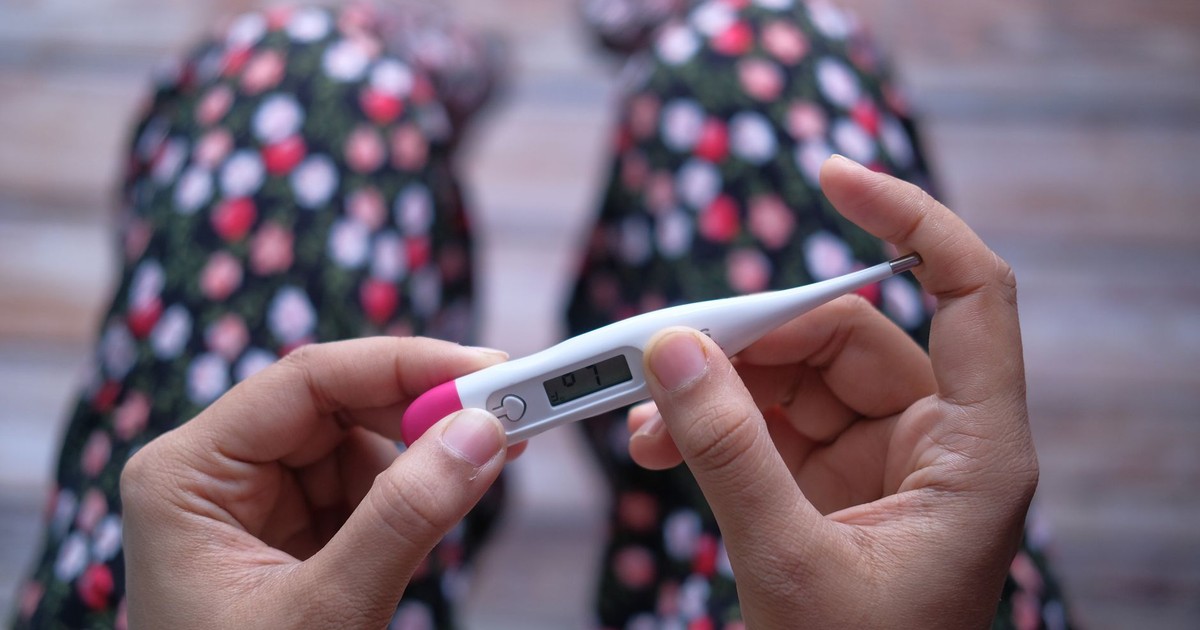 Close-up of hands holding a digital thermometer against a blurred background.