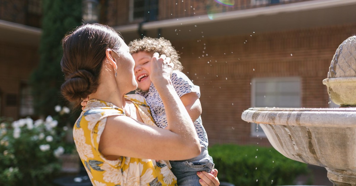 A joyful mother and child share a fun moment near a fountain outdoors.