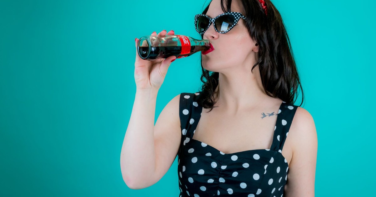 A classic retro pin-up style woman in polka-dot outfit sipping a soda from a glass bottle.