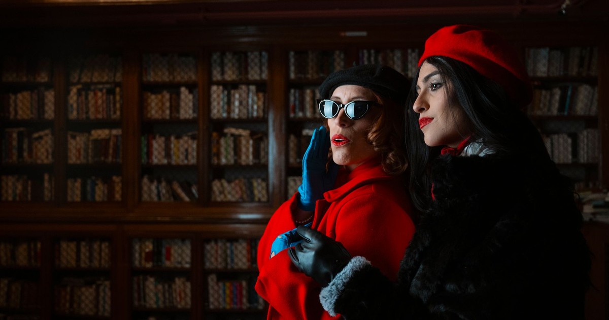 Two fashionable women in a library, wearing retro outfits and posing dramatically.