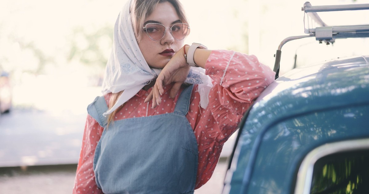 Young woman in stylish attire with sunglasses posing by a vintage car.