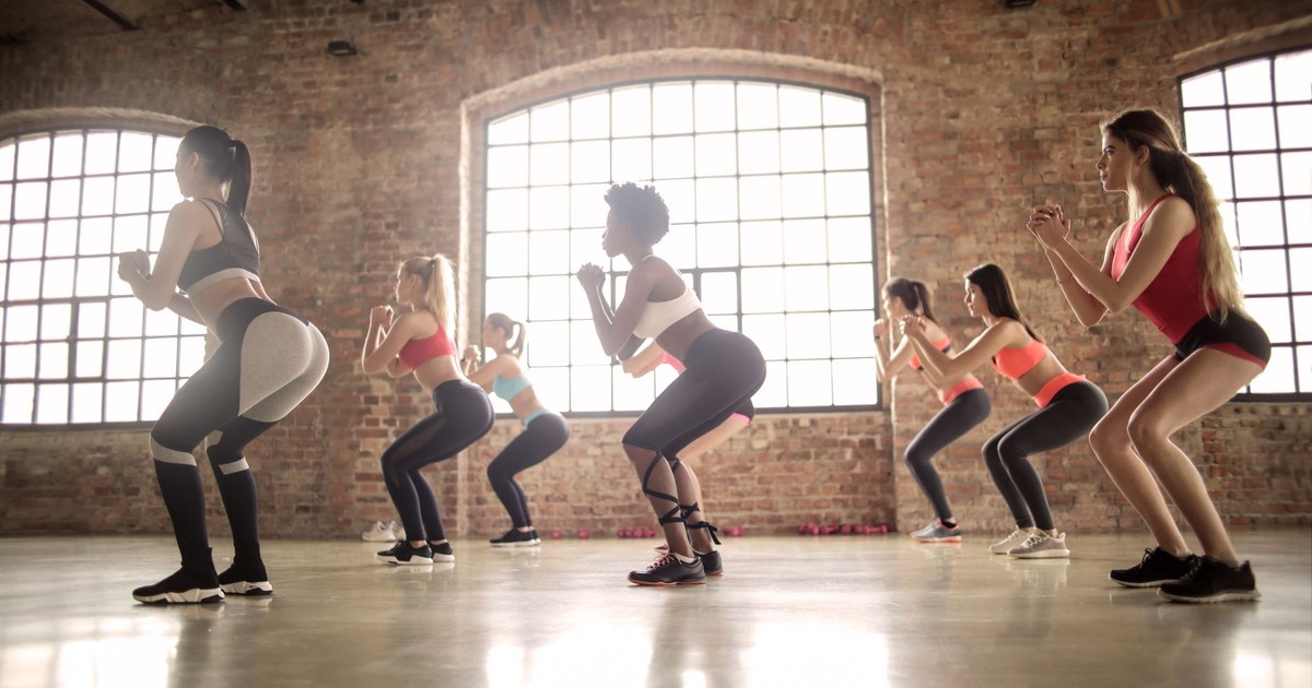 Women participating in a group fitness class performing squats in an industrial-style studio.