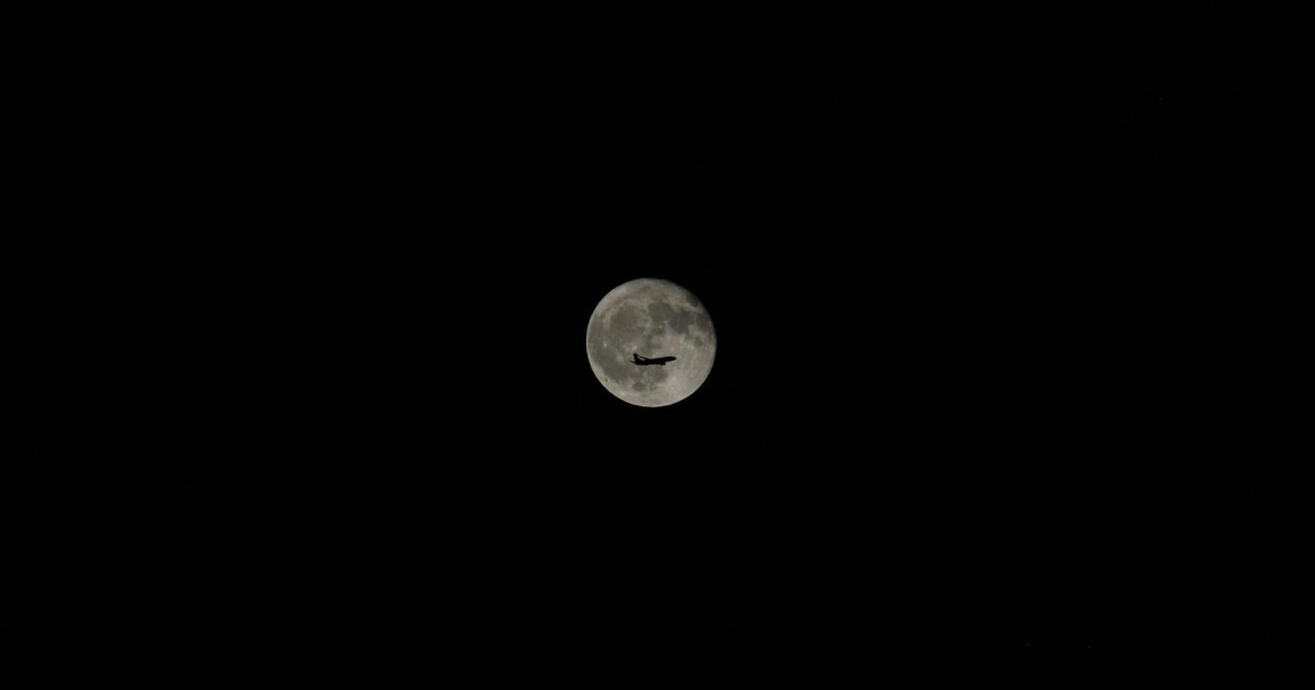 An airplane silhouette against a bright full moon in a clear night sky, showcasing travel and exploration.