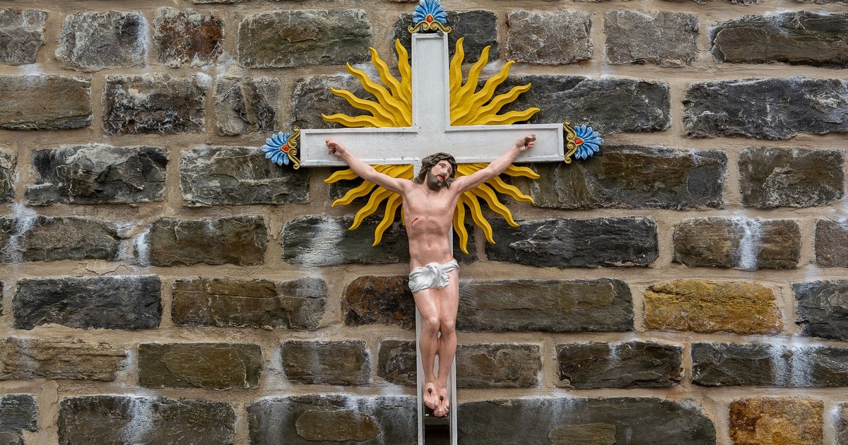 Colorful crucifix with sunburst on an ancient stone wall symbolizing faith.