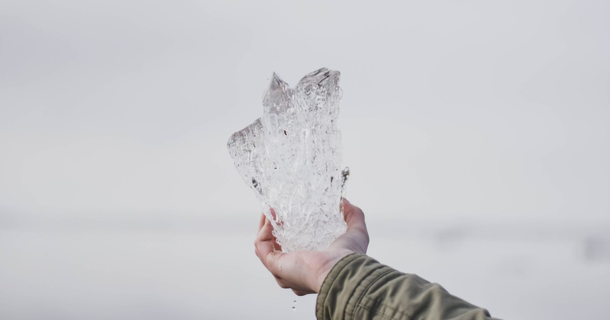 A hand holding a large piece of clear ice against a light background.