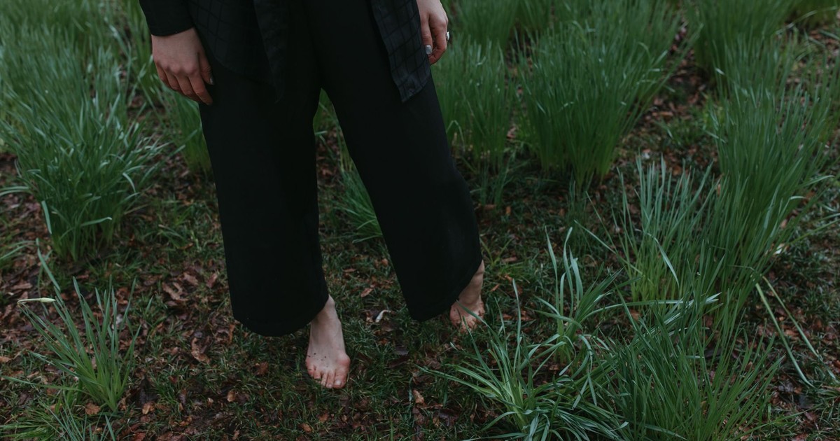 A person standing barefoot in grass, embracing nature with tranquility.