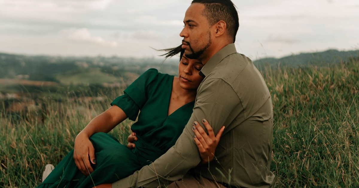 A couple embraces lovingly in a serene meadow landscape, capturing a moment of romance.