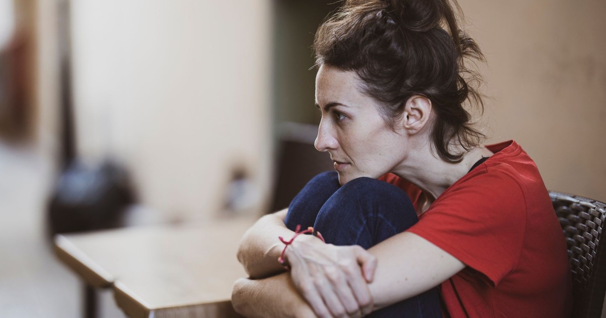A contemplative woman in casual clothes sits indoors, deep in thought.