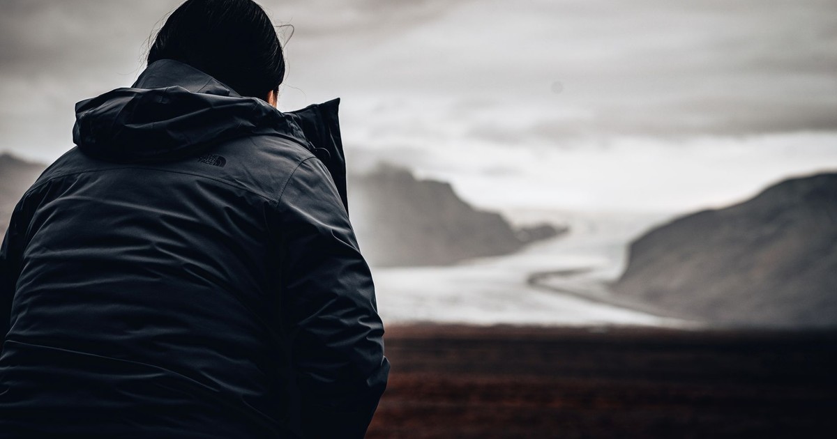 A solitary traveler in winter jacket looking at vast, overcast landscape.