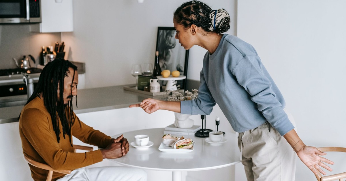Young black woman blaming ethnic depressed boyfriend sitting at table in living room at home