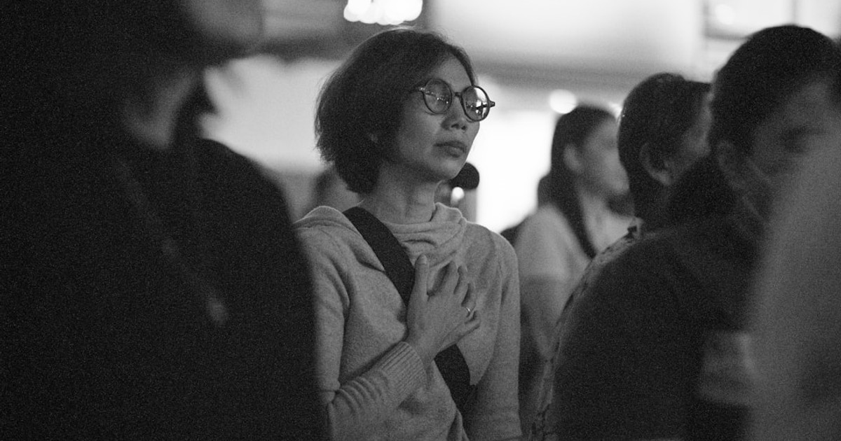 Woman in glasses with hand on chest looking away